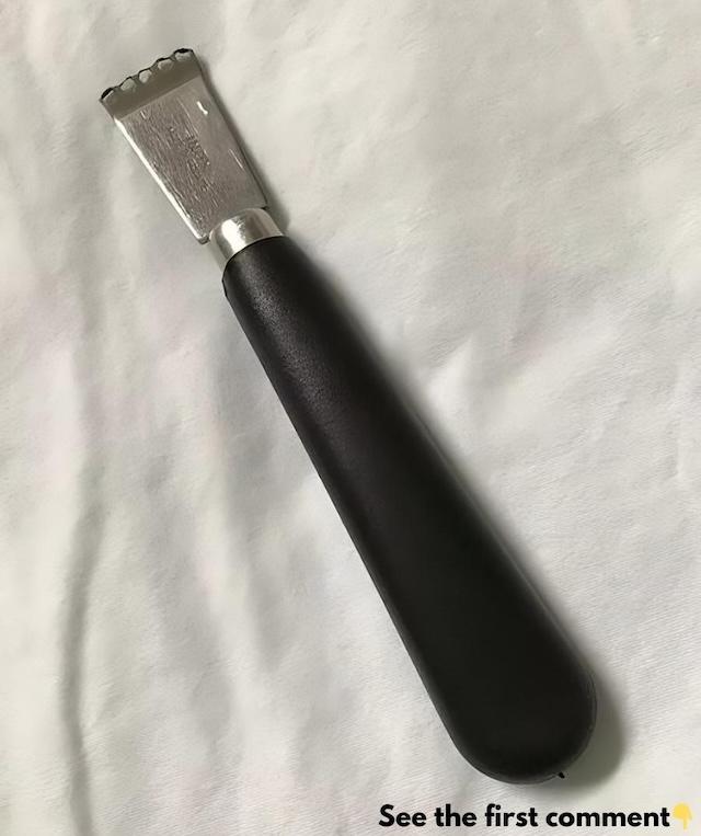 A close-up of a vintage fruit zester, showing its sleek metal head and sturdy black handle, designed for removing the zest of citrus fruits with ease